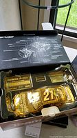 Gold metallic die cast car with number 21 and Motorcraft branding inside original box with owner's documentation and schematic illustration on box lid.