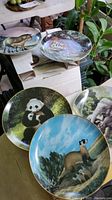 Four animal collector plates showing Black-footed Ferret, Panda, Elephant, and Tiger arranged and photographed together.