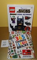 Photo of both LEGO hardcover books: '365 Things To Do With Lego Bricks' showing the activity selector and timer, and the 'Batman Visual Dictionary' with the missing exclusive Electro Suit Batman minifigure.