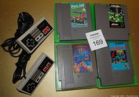 Photo shows 4 Nintendo NES game cartridges (Tetris, Bomberman, Othello, RC Pro Am) and 2 wired NES controllers on a flat surface.