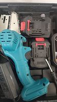 Teal cordless power chainsaw with black and red battery pack inside the carrying case
