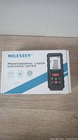 Closed box of MILESEEY Professional Laser Distance Meter on a wood surface showing branding and product image.