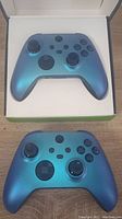 Top view showing two Xbox Aqua Shift controllers, one inside its original box and one outside the box.