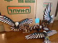 Photo showing three large metal eagles painted in red, white, and blue with stars and stripes, and several small metal soldier figurines arranged on a table with a U-Haul box backdrop.