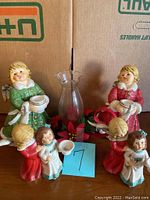 Six Goebel angel figurines arranged around a glass candle holder with red and green Christmas decoration base.