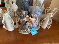 Nativity scene figurine with Mary on donkey, Joseph, and Baby Jesus, flanked by two white angel candle holders with gold accents.