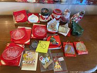 Photo shows various Christmas decorations including boxed glass or plastic ornaments and several ceramic figurines of Santa Claus and snowmen, along with hanging ornaments and a green Christmas tree decoration.