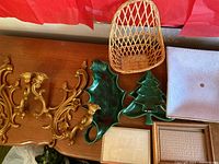Two gold-tone ornate candle sconces on left, wicker basket on top center, green ceramic holly leaf and Christmas tree ceiling light covers in middle, white ceramic dish on right, two wooden 5x7 picture frames in front