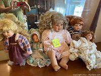 Five porcelain dolls grouped together on a surface in front of a mirror, showing various hair colors, styles, and detailed clothing