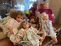 Five vintage-style porcelain dolls displayed together on a table with visible sunlight and furniture in the background.