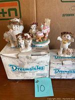 Photo showing six Dreamsicles cherub figurines arranged on two original boxes, with details visible on poses, crowns, and cake centerpiece.