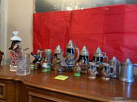 Wide shot of German beer steins and various mugs displayed on a wooden surface with red background.