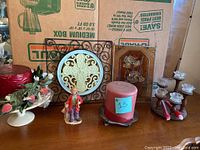 Photo showing various decorative items including hanging plaque with cross, pillar candle, two candle holders with taper candles, pedestal bowl with flowers, and a clown figurine