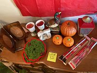 Photo showing the entire lot on a wooden table with red backdrop. Items include ceramic pumpkins, duck figurine on wooden base, red lantern, Christmas candle holders, picture frames, boxed Christmas candles, and knit holiday item.