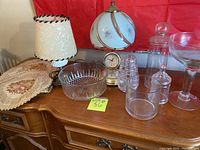 Overview of lot showing lamps, glass bowls, glasses, jars, doilies and candle grouped on wood table