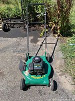 Photo of green Weedeater lawn mower with Briggs & Stratton engine, metal deck, pull start, and handlebar controls on asphalt outdoors.