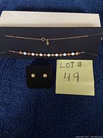 18-inch gold-tone chain necklace with white and gold beads laid out on black fabric, with matching earrings on the side and a note with lot number