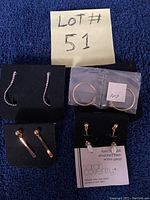 All four pairs of Sarah Coventry post back earrings displayed on jewelry cards and a bag, shown on a dark blue surface with lot number visible.