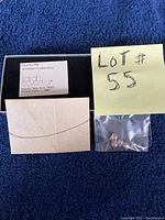 Plastic bag with pink pearl beads and a small sealed paper envelope, alongside a yellow sticky note labelled 'Lot # 55', displayed on a navy blue fabric background.