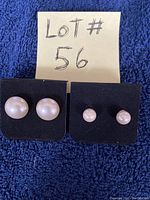 Two sets of Sarah Coventry pearl stud earrings displayed on black cards against blue fabric background, with 'Lot# 56' card above