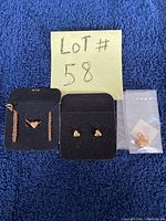 Photo of the lot showing a necklace with a heart pendant on a chain, a pair of heart-shaped post back earrings, and a heart charm in a plastic bag, all displayed on a dark backing against a blue fabric background.
