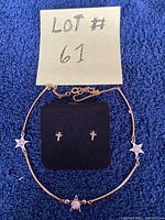Photo of necklace and earrings alongside lot number card on blue fabric background