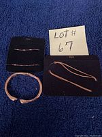 Photo of three gold-toned bracelets arranged on a blue fabric background with a lot number card.