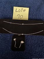 Photo of silver necklace featuring blue sapphire-like and clear stones, laid flat with black background and Lot#70 note