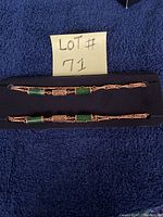 Two images of the gold-tone necklace and bracelet set with green jade-like stones displayed on a dark fabric with a handwritten lot number 71.