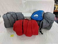 Photo showing three sleeping bags: two large blue Ozark Trail branded bags with compression straps, and one large red sleeping bag without tag needing cleaning.