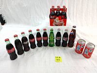 Full collection display with all 13 unopened bottles and cans lined up in front of the Coca-Cola Christmas six-pack