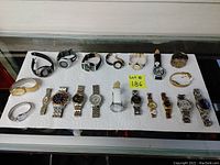 Shot of all 20 wristwatches arranged on white paper towel, varying styles and bands, showing overall lot contents.