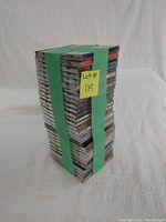 Stack of 30 music CDs secured by green strap viewed from side on white fabric background.