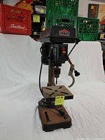 Front view of Jobmate drill press showing adjustable metal table, power switch, and chuck with some dirt and surface rust on base and column.