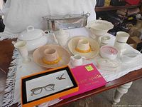 Overview of entire lot showing all kitchen ceramic and metal serveware on a white tablecloth including roasting pot, tureen, sombreros, platters, utensil holders, and Kate Spade key dish in box.