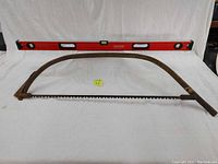 Full view of 48-inch red Craftsman metal level and 38-inch rusted vintage bow saw.