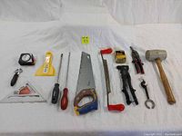 Overview of most tools laid out on white fabric. Visible are tape measure, adjustable wrench, putty knife, screwdrivers, hand saw, clamp, aviation snips, mallet, and hammer.