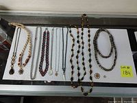 Photo showing all 12 necklaces and pendants laid out on a white surface inside a display case, with variety in styles including chains, beads, and braided designs.