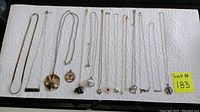 Image showing 12 silver necklaces laid out on a paper towel with various pendants including hearts, clover, elephant, and name bar