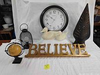 Photo showing all seven items: small black metal basket lamp, decorative globe, wooden BELIEVE plaque, pair of pottery ducks, large black clock, and painted clay candle holder.