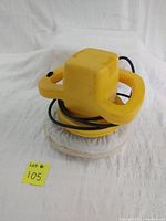 Angle showing the yellow electric polisher with white polishing pad and black power cord on white fabric background.