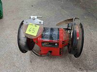 Front view of red PowerMax bench grinder showing grinding wheels with black guards and clear safety shields.