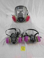 Photo showing one SafetyWord 9900 full face respirator with clear face shield and two pink/yellow filters, along with two Honeywell 5500-30m medium half face respirators with similar pink/yellow filters. All respirators are used with visible dust and attached adjustable straps.
