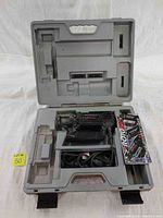 Open molded plastic carrying case with RotoZip Spiral Saw inside charging compartment, power cord coiled, and quick reference guide tucked in side.