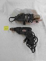 Photo shows Sears Craftsman 4.5 inch sander/grinder with grinding disc attached on top and Jobmate corded power drill below. Both have power cords wrapped around the bodies. Tools rest on white sheet with lot number tag nearby.