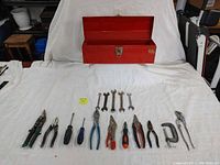 Photo showing the full set of hand tools arranged below an open red metal toolbox, tools include various pliers, wrenches and screwdrivers according to seller description.