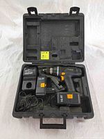 Top-down view inside the black carrying case showing the cordless power drill with an attached battery, spare battery, charger, and storage compartments.