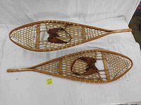 Pair of vintage wooden snowshoes with animal hide webbing and leather straps laid flat side by side.