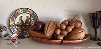 Shelf display with carved wood fruit bowl and carved wood fruits alongside decorative Capri plate, ceramic clogs, carved boy figurine, and glass heart-shaped item.