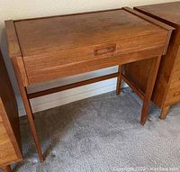 Closed view of wooden vanity desk with splayed legs and hidden lift-top panel